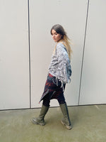 Person wearing a patterned sweater and jeans walking against a plain wall.