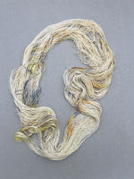 Three skeins of cream-colored yarn with speckles on a gray surface