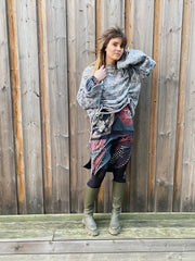 Woman wearing a patterned dress over a gray sweater against a wooden fence.