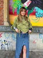 Woman in a green knitted sweater and blue denim skirt standing in front of a colorful mural.